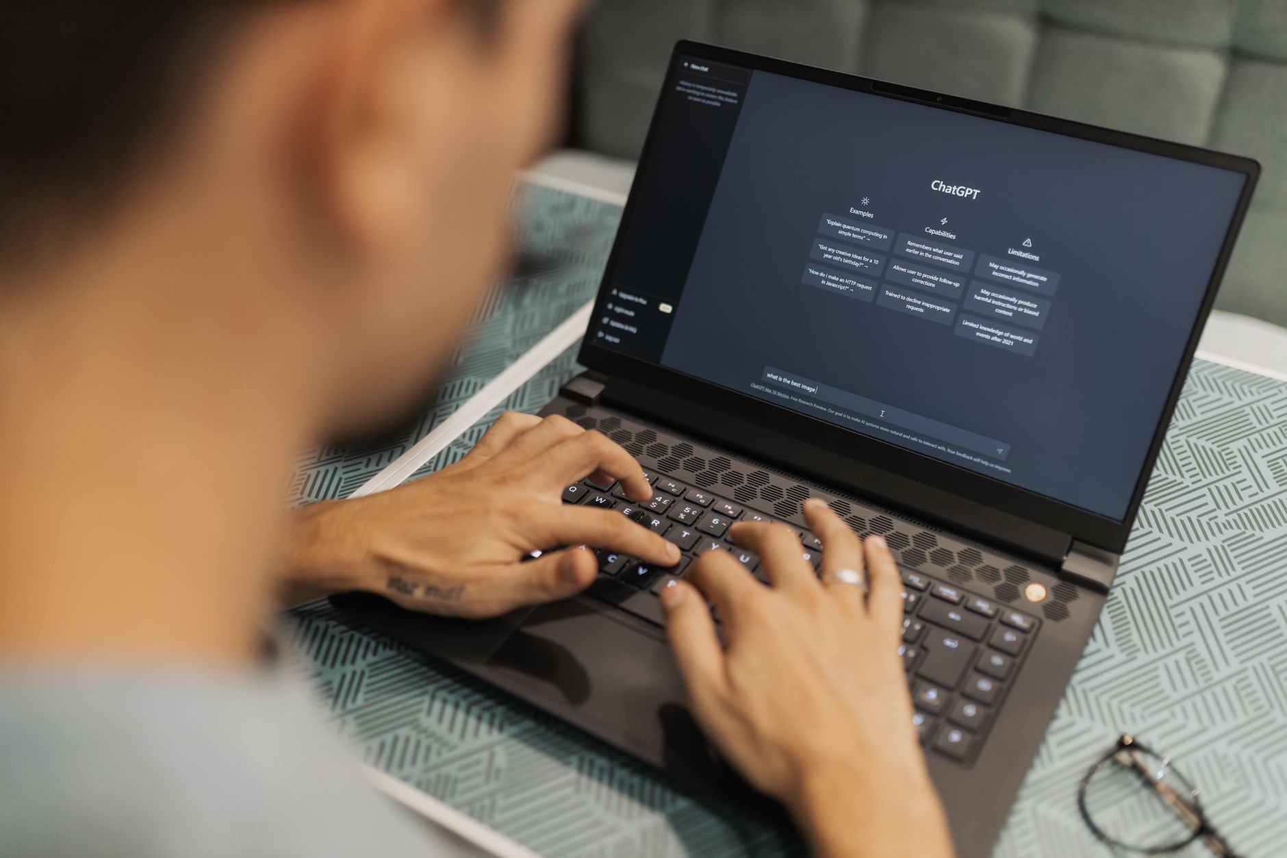 Person typing on laptop showing ChatGPT interface on screen